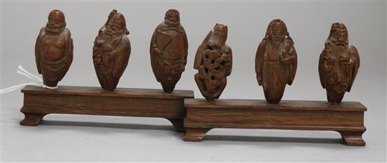 A set of six Chinese peach stones carved as immortals and a monkey, rosewood stands, each approx. height 4cm